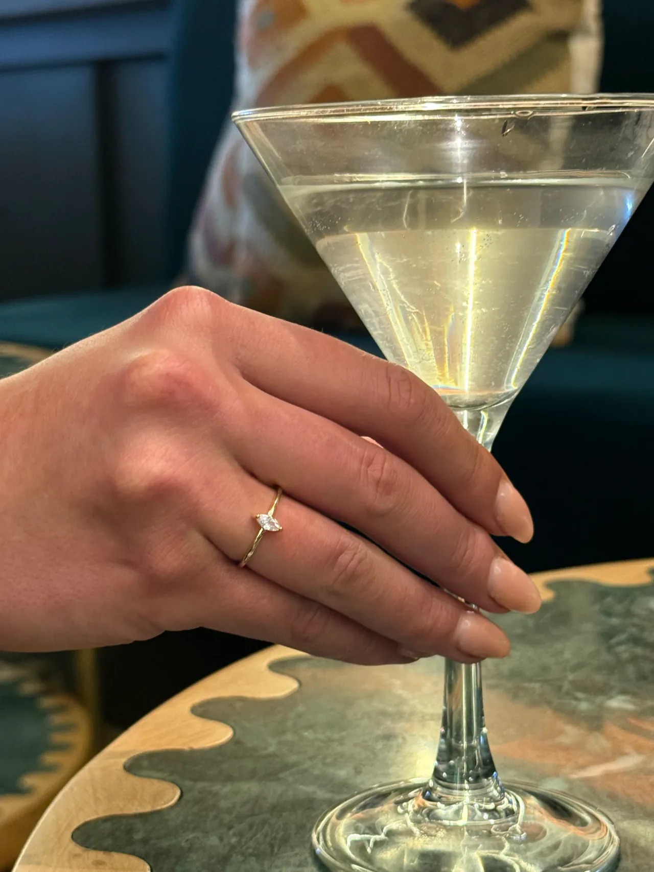 The Astra gold marquise ring on a hand resting around a martini glass